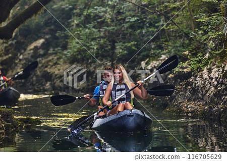 A group of friends enjoying having fun and kayaking while exploring the calm river, surrounding forest and large natural river canyons A group of friends enjoying having fun and kayaking while exploring the calm river, surrounding forest and large natural river canyons 116705629