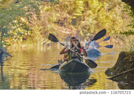 A group of friends enjoying having fun and kayaking while exploring the calm river, surrounding forest and large natural river canyons A group of friends enjoying having fun and kayaking while exploring the calm river, surrounding forest and large natural river canyons 116705723