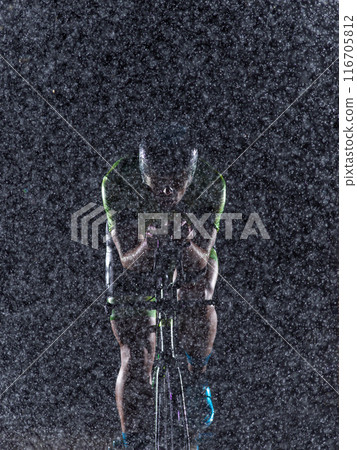 A triathlete braving the rain as he cycles through the night, preparing himself for the upcoming marathon. The blurred raindrops in the foreground and the dark, moody atmosphere in the background add A triathlete braving the rain as he cycles through the night, preparing himself for the upcoming marathon. The blurred raindrops in the foreground and the dark, moody atmosphere in the background add 116705812