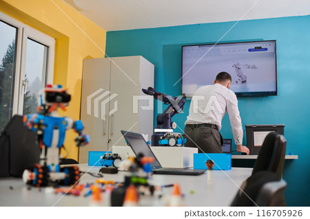 A student testing his new invention of a robotic arm in the laboratory, showcasing the culmination of his research and technological prowess. 116705926