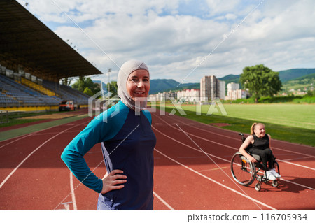 A Muslim woman wearing a burqa resting with a woman with disability after a hard training session on the marathon course 116705934
