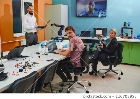 A group of colleagues working together in a robotics laboratory, focusing on the intricate fields of robotics and 3D printing. Showcase their dedication to innovation, as they engage in research 116705953