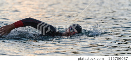 A professional triathlete trains with unwavering dedication for an upcoming competition at a lake, emanating a sense of athleticism and profound commitment to excellence. 116706087