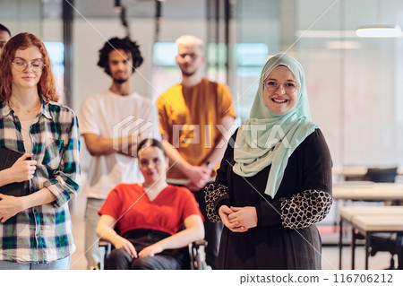 A diverse group of young business people congregates within a modern startup's glass-enclosed office, featuring inclusivity with a person in a wheelchair, an African American young man , and a hijab A diverse group of young business people congregates within a modern startup's glass-enclosed office, featuring inclusivity with a person in a wheelchair, an African American young man , and a hijab 116706212