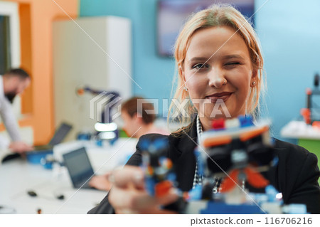 A woman wearing a protective mask standing in a laboratory while her colleagues test a new robotic invention in the background. A woman wearing a protective mask standing in a laboratory while her colleagues test a new robotic invention in the background. 116706216