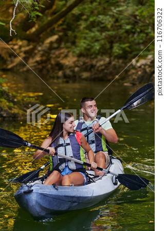 A young couple enjoying an idyllic kayak ride in the middle of a beautiful river surrounded by forest greenery 116706322