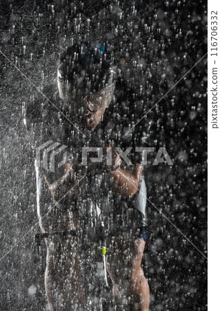 A triathlete braving the rain as he cycles through the night, preparing himself for the upcoming marathon. The blurred raindrops in the foreground and the dark, moody atmosphere in the background add A triathlete braving the rain as he cycles through the night, preparing himself for the upcoming marathon. The blurred raindrops in the foreground and the dark, moody atmosphere in the background add 116706332