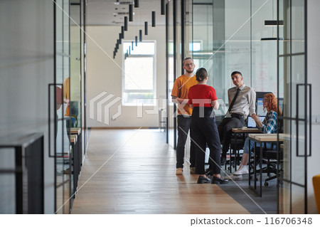 A business group, including an African American businessman in a wheelchair, collaborates within a modern glass office, actively engaged around a computer and laptop, collectively solving diverse 116706348