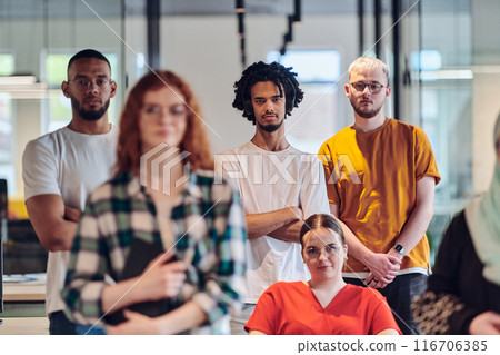 A diverse group of business people walking a corridor in the glass-enclosed office of a modern startup, including a person in a wheelchair and a woman wearing a hijab, showing a dynamic mix of 116706385