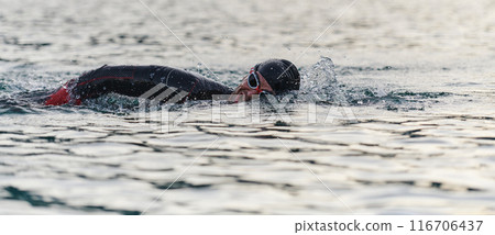 A professional triathlete trains with unwavering dedication for an upcoming competition at a lake, emanating a sense of athleticism and profound commitment to excellence. 116706437