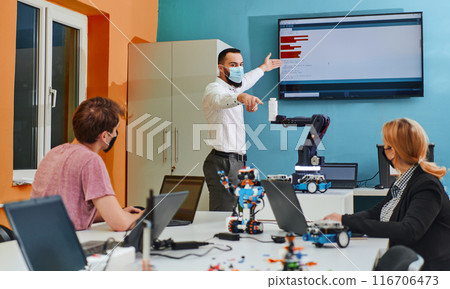 A group of colleagues working together in a robotics laboratory, focusing on the intricate fields of robotics and 3D printing. Showcase their dedication to innovation, as they engage in research 116706473