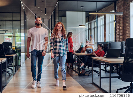 A young African American businessman and a modern businesswoman with orange hair stand side by side, arms crossed, exuding confidence and unity in a contemporary office setting, epitomizing dynamic 116706556