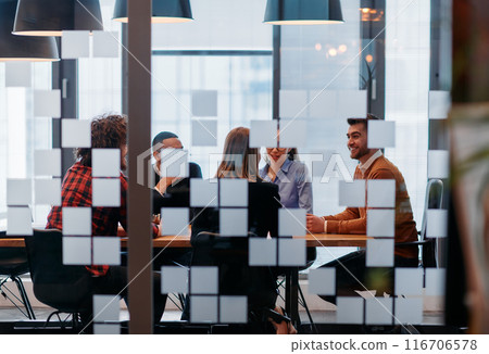 In a sleek glass office space, a team of business professionals engage in lively discussions and exchange strategic ideas, showcasing collaboration and innovation at the heart of modern corporate 116706578