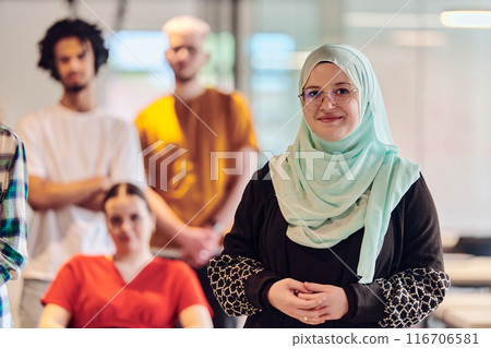A diverse group of young business people congregates within a modern startup's glass-enclosed office, featuring inclusivity with a person in a wheelchair, an African American young man , and a hijab A diverse group of young business people congregates within a modern startup's glass-enclosed office, featuring inclusivity with a person in a wheelchair, an African American young man , and a hijab 116706581