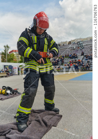 A firefighter dons the essential components of their professional gear, embodying resilience, commitment, and readiness as they gear up for a hazardous firefighting mission, a testament to their 116706763