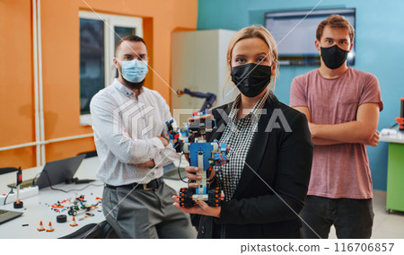 A group of colleagues working together in a robotics laboratory, focusing on the intricate fields of robotics and 3D printing. Showcase their dedication to innovation, as they engage in research 116706857