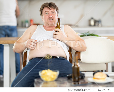 Overweight man with obese belly overeating and drinking beer. Bad habits, eating disorder, alcoholism 116706930