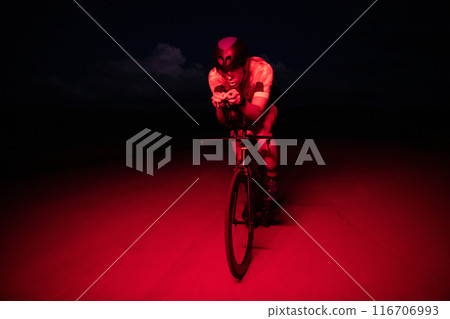 A triathlete rides his bike in the darkness of night, pushing himself to prepare for a marathon. The contrast between the darkness and the light of his bike creates a sense of drama and highlights the A triathlete rides his bike in the darkness of night, pushing himself to prepare for a marathon. The contrast between the darkness and the light of his bike creates a sense of drama and highlights the 116706993