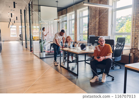 A diverse group of business professionals collaborates in a modern startup coworking center, utilizing a mix of paper-based and technological tools such as mobile phones and computers to collectively 116707013