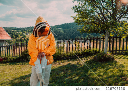 Beekeeper put on a protective beekeeping suit and preparing to enter the apiary Beekeeper put on a protective beekeeping suit and preparing to enter the apiary 116707138