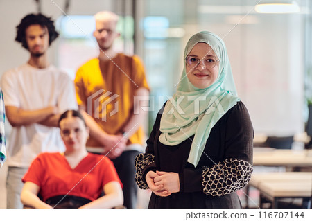 A diverse group of young business people congregates within a modern startup's glass-enclosed office, featuring inclusivity with a person in a wheelchair, an African American young man , and a hijab A diverse group of young business people congregates within a modern startup's glass-enclosed office, featuring inclusivity with a person in a wheelchair, an African American young man , and a hijab 116707144
