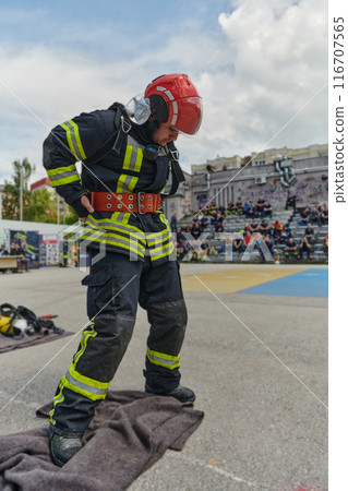 A firefighter dons the essential components of their professional gear, embodying resilience, commitment, and readiness as they gear up for a hazardous firefighting mission, a testament to their 116707565