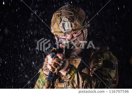 Army soldier in Combat Uniforms with an assault rifle, plate carrier and combat helmet going on a dangerous mission on a rainy night. 116707596