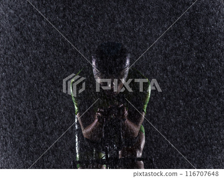 A triathlete braving the rain as he cycles through the night, preparing himself for the upcoming marathon. The blurred raindrops in the foreground and the dark, moody atmosphere in the background add A triathlete braving the rain as he cycles through the night, preparing himself for the upcoming marathon. The blurred raindrops in the foreground and the dark, moody atmosphere in the background add 116707648