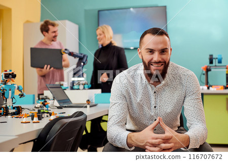 A man sitting in a robotics laboratory while his colleagues in the background test new, cutting edge robotic inventions. A man sitting in a robotics laboratory while his colleagues in the background test new, cutting edge robotic inventions. 116707672