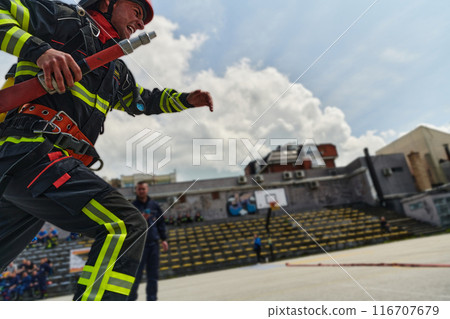 In a dynamic display of synchronized teamwork, firefighters hustle to carry, connect, and deploy firefighting hoses with precision, showcasing their intensive training and readiness for challenging 116707679