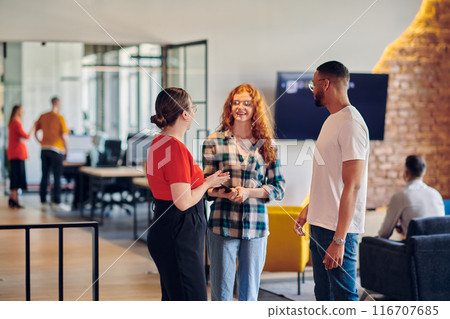 A group of young business individuals, including a girl with orange hair and an African American man, stands in a modern corporate hallway, collectively examining business progress on a smartphone A group of young business individuals, including a girl with orange hair and an African American man, stands in a modern corporate hallway, collectively examining business progress on a smartphone 116707685