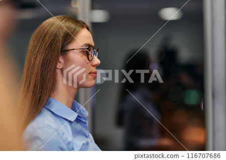 Confident Businesswoman in Glasses and Blue Shirt Engaged in Office Discussion Confident Businesswoman in Glasses and Blue Shirt Engaged in Office Discussion 116707686