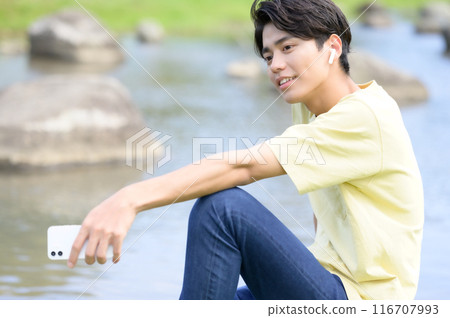 A man operating his smartphone while cooling off by the water in summer 116707993
