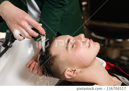 Barber shampooing washing a male clients head in the sink. 116708517