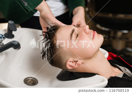 Barber shampooing washing a male clients head in the sink. 116708519