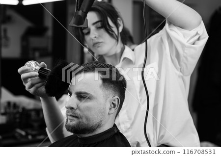 The hairdresser sweeps the hair during the haircut with a brush and drying air. The hairdresser sweeps the hair during the haircut with a brush and drying air. 116708531