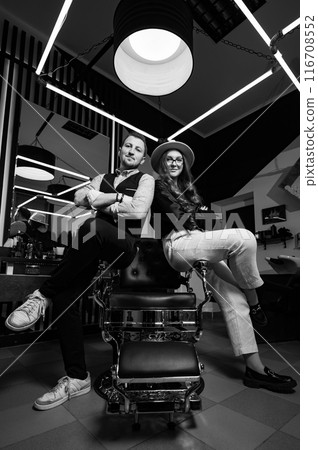 A couple of barbers sit on a chair in a modern interior of a barbershop. A couple of barbers sit on a chair in a modern interior of a barbershop. 116708552