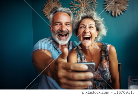 An elderly couple captures joyful moments at home using a smartphone, embracing modern technology for shared memories and social media moments.Generated image 116709113