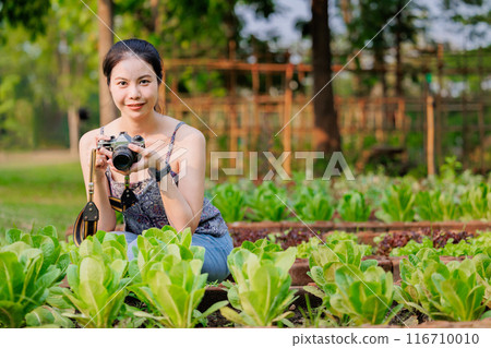 happy asian women with camera in vegetable garden agriculture plant farm, eco green farming travel concept. happy asian women with camera in vegetable garden agriculture plant farm, eco green farming travel concept. 116710010