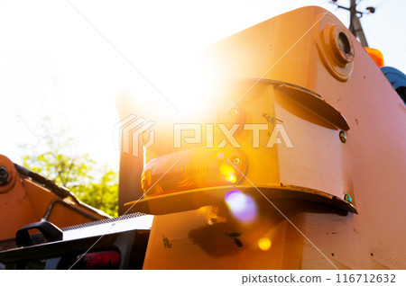 Close-up view of an excavator from behind with sun glare. Tail lights of a small excavator Close-up view of an excavator from behind with sun glare. Tail lights of a small excavator 116712632