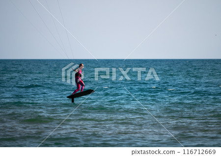 woman at sea rides a hydrofoil surfboard using a kite wing. Extreme sport, fast travel across the sea on a board 116712669