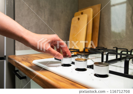Gas stove. Turning the gas burner on and off. A woman's hand reaches out to cook, the beginning of the food preparation process Gas stove. Turning the gas burner on and off. A woman's hand reaches out to cook, the beginning of the food preparation process 116712708