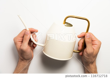 Gardening concept. A man holds a yellow watering can in his hands on a white background, close-up top view Gardening concept. A man holds a yellow watering can in his hands on a white background, close-up top view 116712718