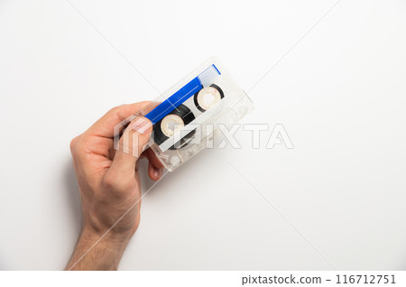 An unrecognizable male hand holds a retro audio cassette on a white background. Using magnetic audio cassettes 116712751