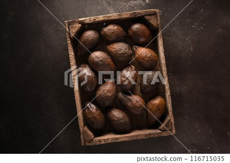 Top view of an old brown avocado in a wooden box on a black background in rustic style. The concept of aging, storage and spoilage of fruits, as well as a beautiful textured background. 116715035