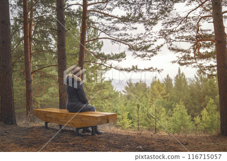 A woman relaxes on a bench in a pine forest, admiring the mountain view and peaceful surroundings A woman relaxes on a bench in a pine forest, admiring the mountain view and peaceful surroundings 116715057