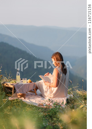 A woman enjoys reading a book in a peaceful and scenic mountain view during a picnic 116715156
