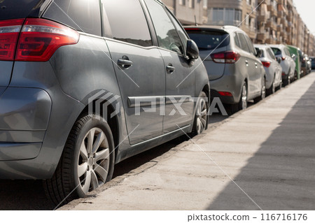 Row of diverse cars parked along urban street, illustrating the typical scene in city parking zone. Ideal for urban planning articles, parking management content, transportation theme illustrations. 116716176