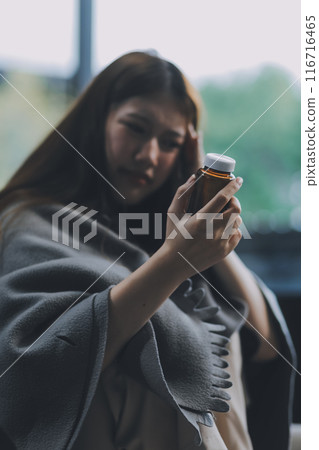 A woman with a cold with pills is treated at home chooses which drugs to take and self-medicates, checks the expiration date while sitting on the couch at home 116716465