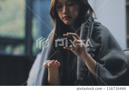 A woman with a cold with pills is treated at home chooses which drugs to take and self-medicates, checks the expiration date while sitting on the couch at home 116716466